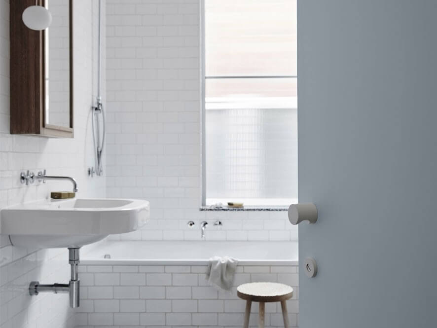 Sleek White Tiled Bathroom with Wooden Framed Mirror and Bathtub Near Window and Blue Door